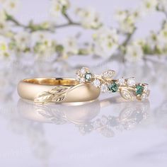 two gold wedding rings with green and white stones on them sitting next to each other