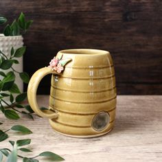 a yellow ceramic mug sitting on top of a table next to a potted plant