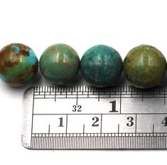 four different colored beads sitting next to a ruler