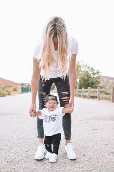 a woman holding the hand of a toddler who is wearing ripped jeans and white sneakers