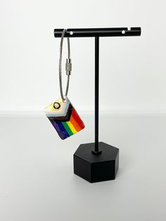 a pair of earrings is hanging from a black stand on a white surface with a rainbow square in the center