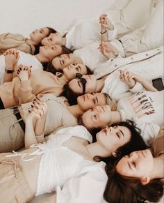 four women laying on the bed with their arms in the air and looking at the camera