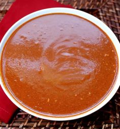 a white bowl filled with red sauce on top of a woven table cloth next to a wooden spoon