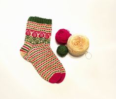 two balls of yarn are next to a pair of socks with red and green designs