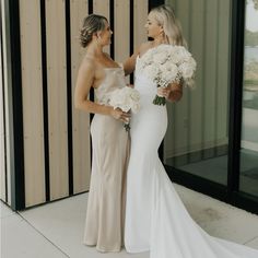 two women standing next to each other in front of a building holding bouquets of flowers