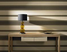 a table with a lamp on it in front of a striped wallpapered room