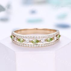 two wedding bands with green and white stones on top of each other in front of a box