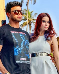 a man and woman standing next to each other in front of palm trees with sunglasses on