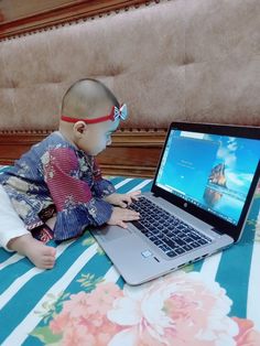 a baby is sitting on the bed with a laptop in front of him and looking at the screen