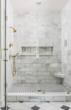 a walk in shower sitting next to a white tiled wall and floor with gold fixtures