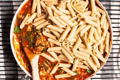 a pan filled with pasta and sauce on top of a table next to a wooden spoon