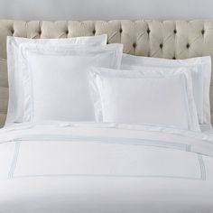 a bed with white sheets and pillows on top of it, in front of a beige headboard