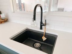 a kitchen sink with a black faucet and white counter top next to a window