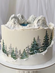 there is a cake decorated with trees and mountains on the top, along with frosting