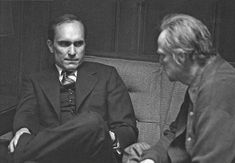 black and white photograph of two men in suits sitting on a couch, facing each other