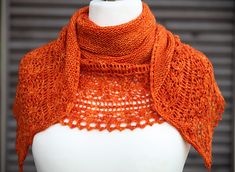 an orange knitted shawl on top of a white mannequin headdress