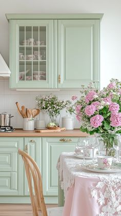 a kitchen with green cabinets and pink flowers on the table