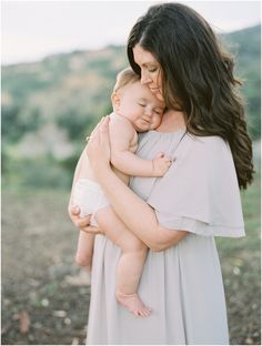 a woman holding a baby in her arms while she is wearing a dress and smiling at the camera