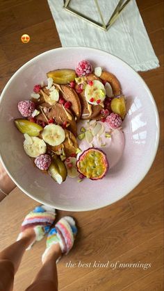 a white bowl filled with fruit and nuts on top of a wooden table next to a woman's hand