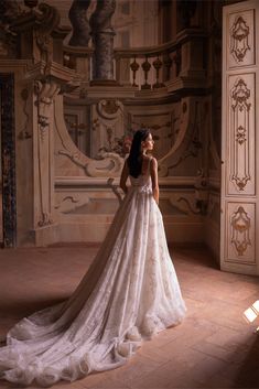 a woman in a wedding dress is standing near a wall and looking off into the distance