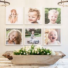 a bowl with flowers in it sitting on a table next to pictures hanging on the wall