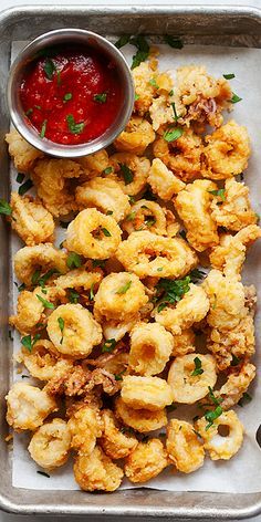 a tray filled with fried food next to a bowl of ketchup and dipping sauce