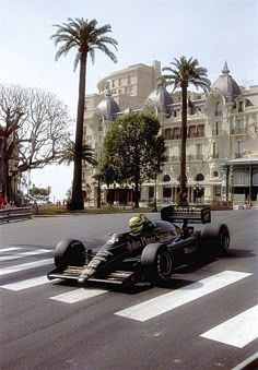 a man driving a race car down a street next to tall buildings and palm trees