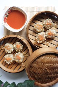 three wooden baskets filled with dumplings next to a bowl of soup and green leaves