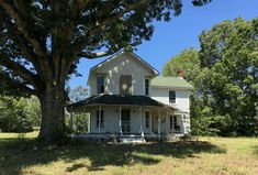 an old white house sitting on top of a lush green field next to a tree