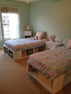 two beds in a room with green walls and carpeted flooring, one has pink pillows on it