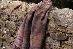 a brown scarf hanging on a stone wall next to a rock wall with trees in the background