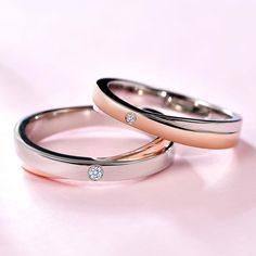 two gold wedding bands with diamonds on them sitting next to each other in front of a pink background