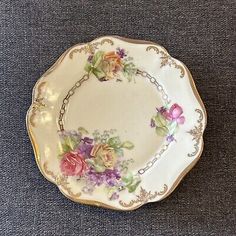 an antique porcelain plate with flowers on the rim and gold trimmings, sitting on a blue surface