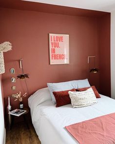 a white bed topped with pillows next to a red wall and pictures on the wall