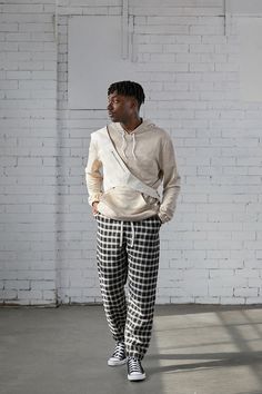 a man standing in front of a white brick wall with his hands in his pockets