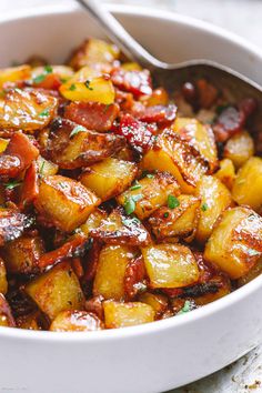 a white bowl filled with cooked potatoes and bacon on top of a table next to a fork