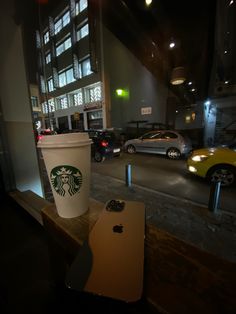 a starbucks cup sitting on top of a wooden table next to a parking lot filled with cars