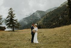 a bride and groom standing in front of a ski lift at the bottom of a mountain