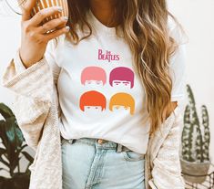 a woman holding a cup and wearing a t - shirt with the beatles on it