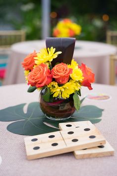 a vase filled with yellow and red flowers next to two dominos on top of a table