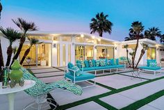 a patio with chairs and palm trees in front of a white house at night time