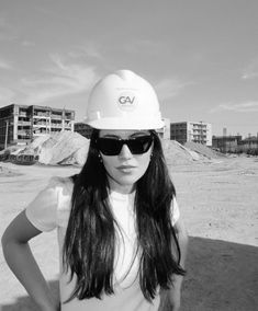 a woman wearing a hard hat and sunglasses standing in the sand with her hands on her hips