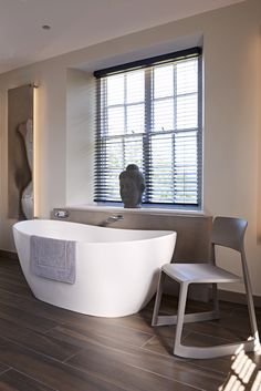 a large white bath tub sitting next to a window in a room with wooden floors