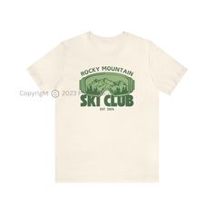 Introducing our exclusive Rocky Mountain Ski Club Graphic T-Shirt - the perfect fusion of comfort and style for winter lovers, skiing enthusiasts, and those who appreciate trendy apparel. Available in a variety of 10 vibrant colors, this T-shirt features a unique design on the front, showcasing the iconic Rocky Mountain ski club emblem, accompanied by a graphic of ski goggles and a stunning mountain landscape. Whether you're gearing up for a day on the slopes, embarking on an adventure, or simply enjoying a leisurely day at home, this unisex T-shirt is the ideal choice. Its versatile fit ensures a comfortable and relaxed feel, allowing you to express your passion for winter and the Rocky Mountains effortlessly. Crafted to cater to your individual style, this T-shirt offers the perfect canv Sporty Logo Print T-shirt For Outdoor Activities, Sporty T-shirt With Logo For Outdoor Activities, Sporty Graphic Print Winter T-shirt, Sporty Graphic Print T-shirt For Winter, White T-shirt For Outdoor Winter Activities, Sporty Top For Ski Season, Sporty Tops For Ski Season, Casual Graphic Print Tops For Winter Sports, Casual Graphic Print Top For Skiing