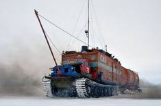 a large orange and blue boat floating on top of snow covered ground in the middle of winter