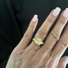 a woman's hand with a yellow diamond ring on her left and pink fingernails