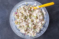 a glass bowl filled with tuna salad next to a yellow plastic spoon on a black surface