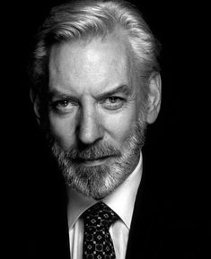 a black and white photo of a man in a suit with a beard wearing a tie