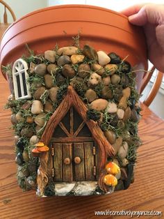 a clay pot with a house made out of rocks and mushrooms on it sitting on a table