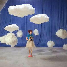 a woman standing in front of a blue backdrop with white clouds floating over her head